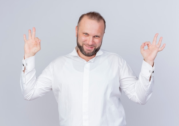 Free Photo bearded man wearing white shirt happy and positive smiling making ok sign standing over white wall