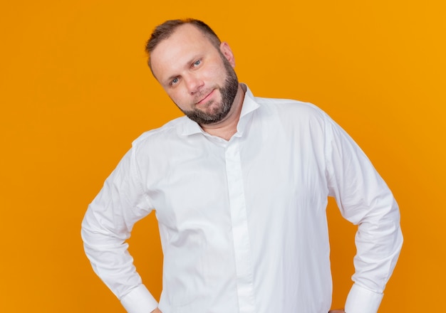 Free photo bearded man wearing white shirt  smiling confident standing over orange wall