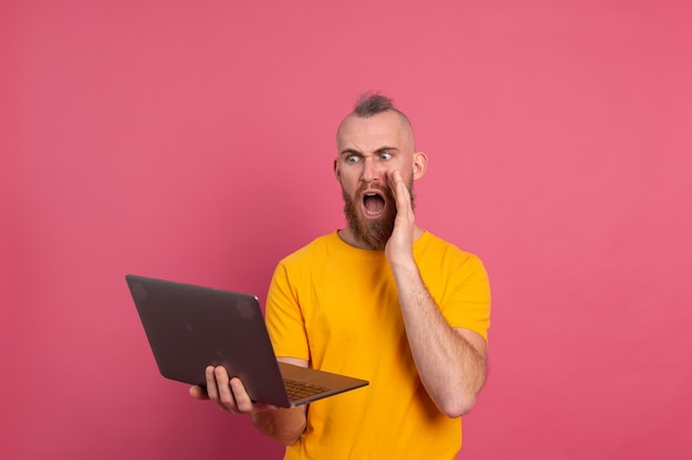 Free Photo bearded man with laptop isolated shock emotions screaming on pink background