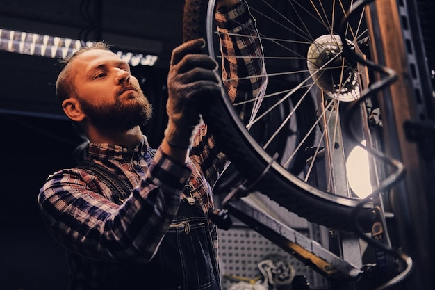 Bearded mechanic doing bicycle wheel service manual in a workshop.