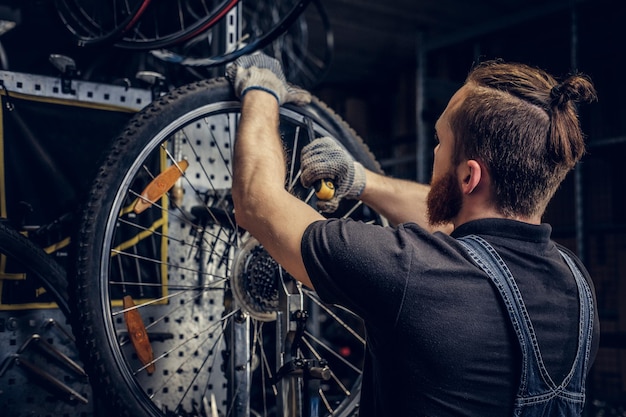 Bearded mechanic repairing bicycle wheel tire in a workshop. Back view, service manual.