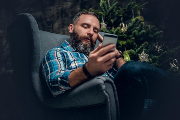 Bearded middle age male using smartphone over Christmas decorated background.