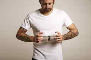 Free photo bearded and tattooed young man in blank white cotton t-shirt holding an empty light gray clear aeropress