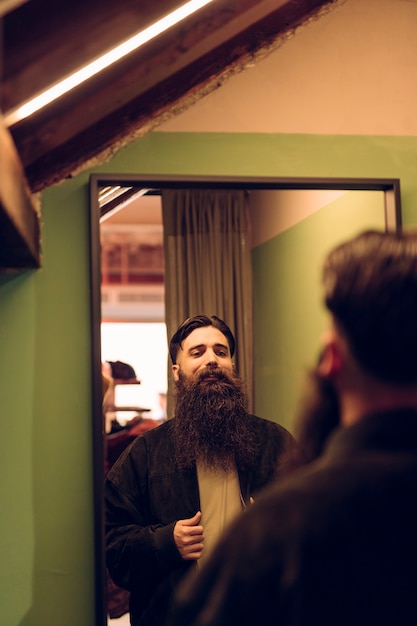 Free photo bearded young man trying jacket in front of mirror