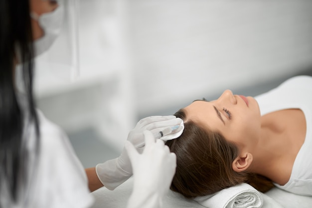 Beautician in protective mask doing procedure for hair