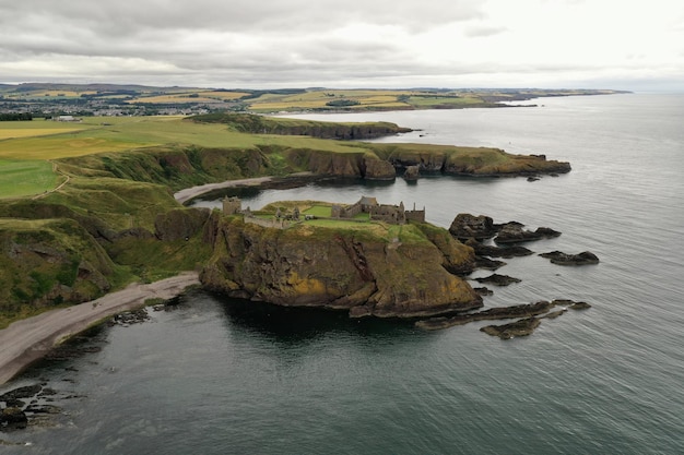 Free Photo beautiful aerial view of high green hills and rocks next to the water under a gray cloudy sky