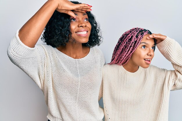 Beautiful african american mother and daughter wearing casual clothes and hugging very happy and smiling looking far away with hand over head. searching concept.