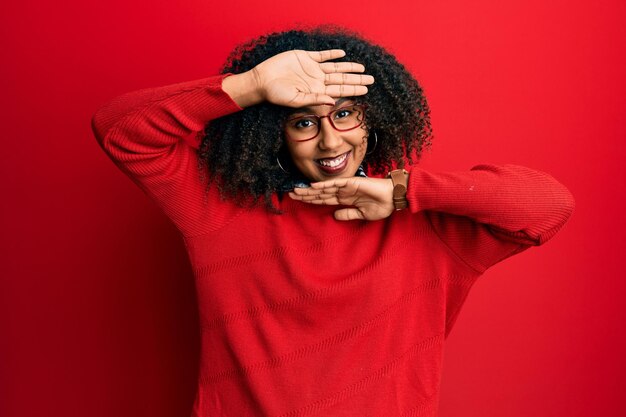 Beautiful african american woman with afro hair wearing sweater and glasses smiling cheerful playing peek a boo with hands showing face. surprised and exited