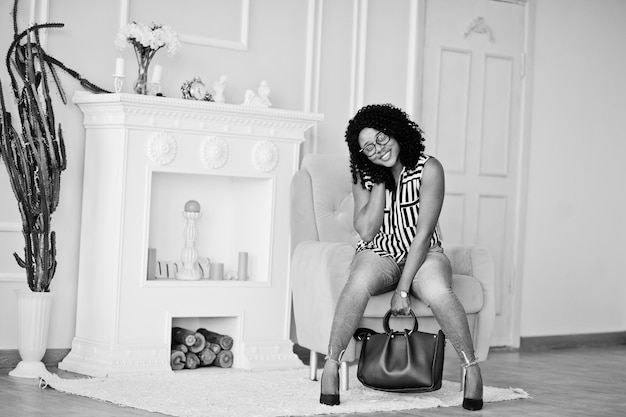 Free photo beautiful african american woman with curly afro hair and eyeglasses handbag posed in room sitting on yellow chair