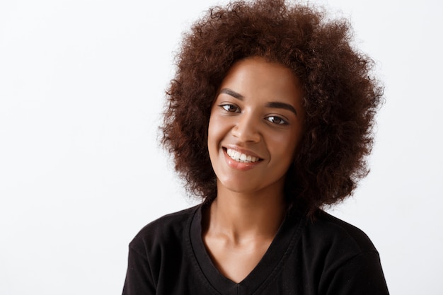 Beautiful african girl smiling over light wall.