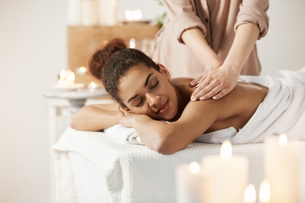 Beautiful african woman smiling enjoying massage with closed eyes in spa salon.