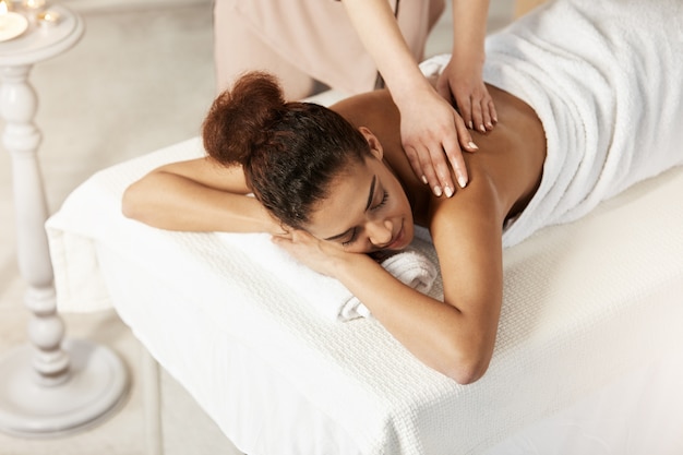 Beautiful african woman smiling enjoying massage with closed eyes in spa salon.