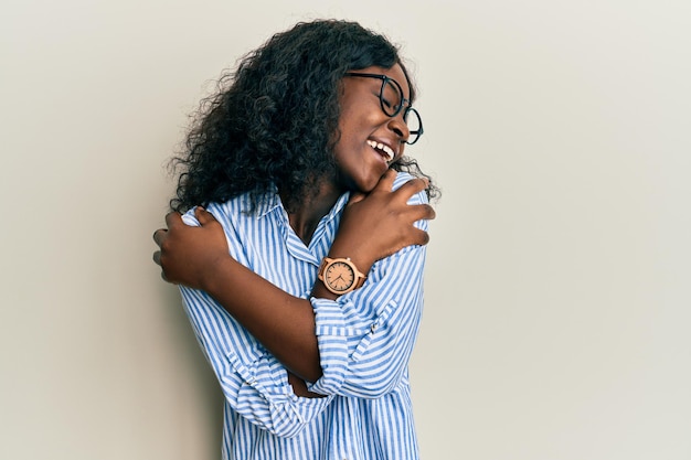 Free photo beautiful african young woman wearing casual clothes and glasses hugging oneself happy and positive, smiling confident. self love and self care