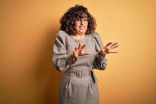 Free photo beautiful arab business woman wearing dress and glasses standing over yellow background disgusted expression displeased and fearful doing disgust face because aversion reaction