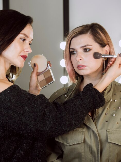 Beautiful artist applying blush on model