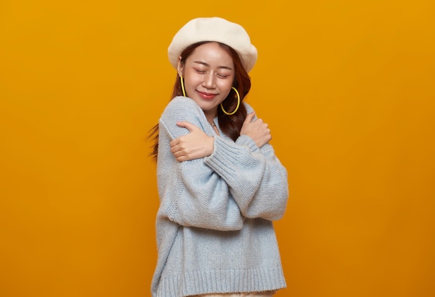 Beautiful Asian teenager woman hugging and embracing herself isolated on studio yellow background