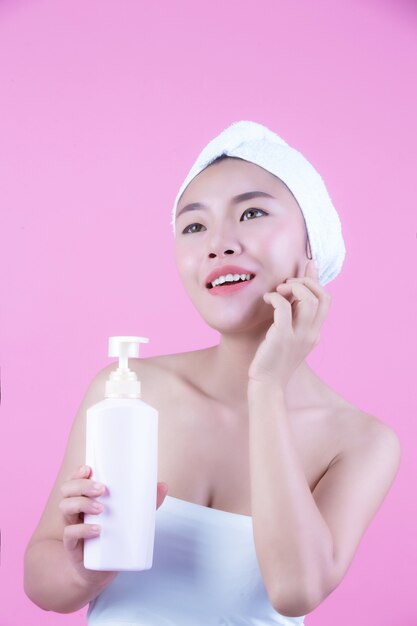 Beautiful Asian woman holding a bottle of product on a pink background.