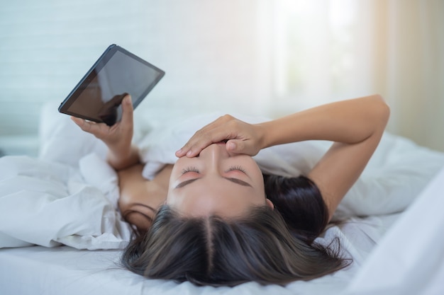 A beautiful Asian woman relaxes and works with a laptop computer, reading at home.