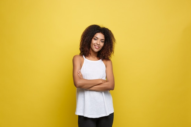 Free photo beautiful attractive african american woman posting play with her curly afro hair. yellow studio background. copy space.