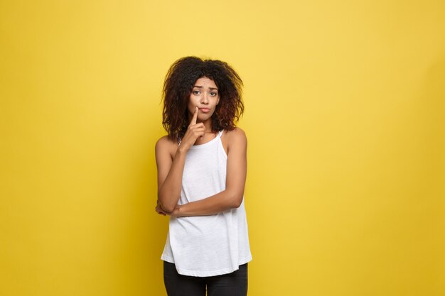 Beautiful attractive African American woman posting play with her curly afro hair. Yellow studio background. Copy Space.