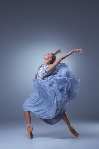 The beautiful ballerina dancing in long blue dress on blue background