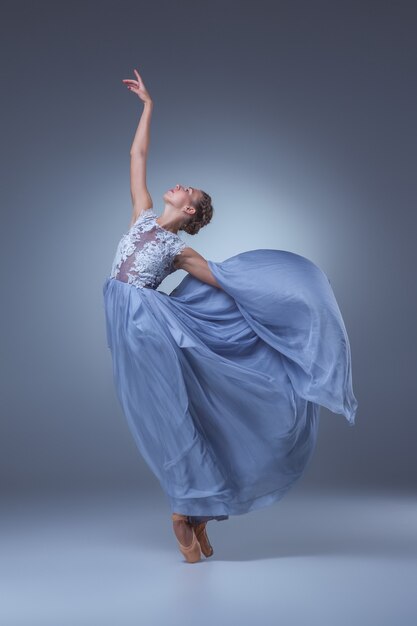 The beautiful ballerina dancing in long blue dress on blue background