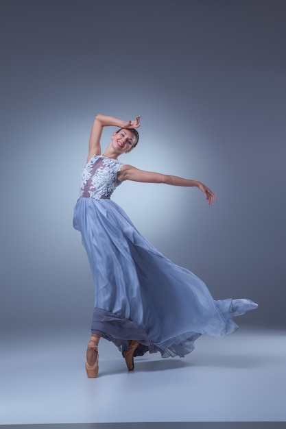 The beautiful ballerina dancing in long blue dress on blue background