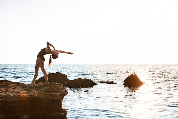 Beautiful ballerina dancing, posing on rock at beach, sea views.