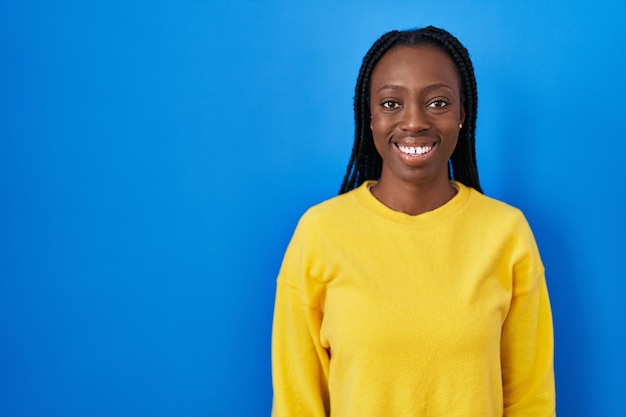 Beautiful black woman standing over blue background with a happy and cool smile on face. lucky person.