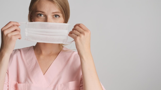 Beautiful blond nurse wearing medical mask on camera with place for advertisement or promotional text near over white background