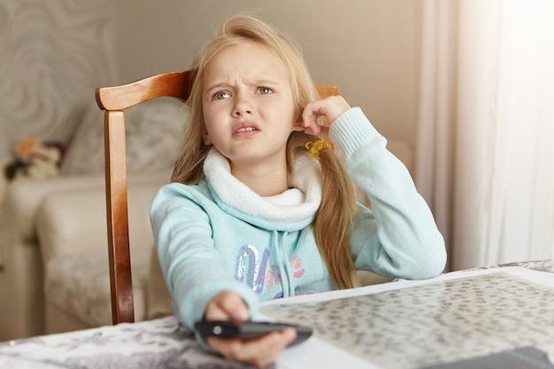 Beautiful blonde Caucasian little girl sitting on chair in living room