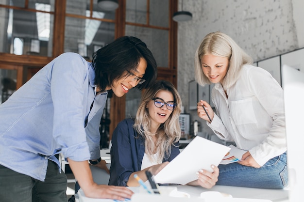 Free Photo beautiful blonde girl in glasses showing report to asian colleague which standing beside her table