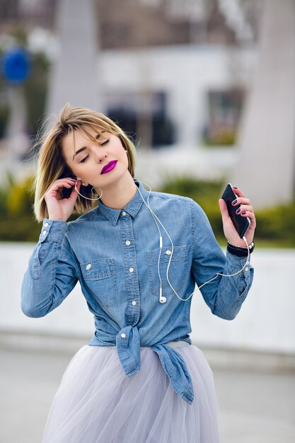 Beautiful blonde girl standing, listening to music and dreaming with closed eyes.