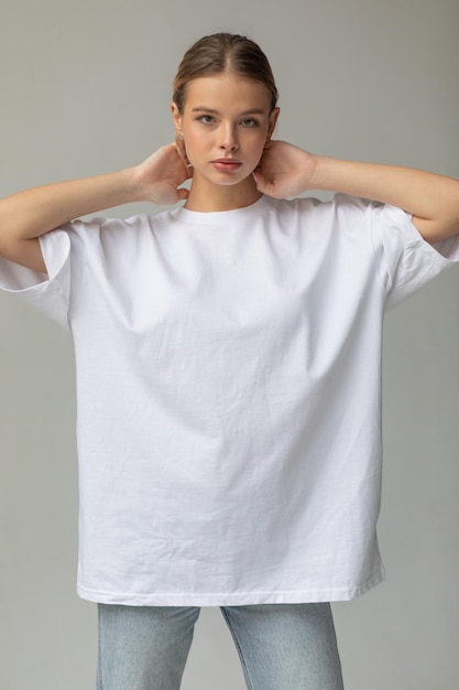 Free photo beautiful blonde girl in a white oversized tshirt and blue jeans posing on a gray background