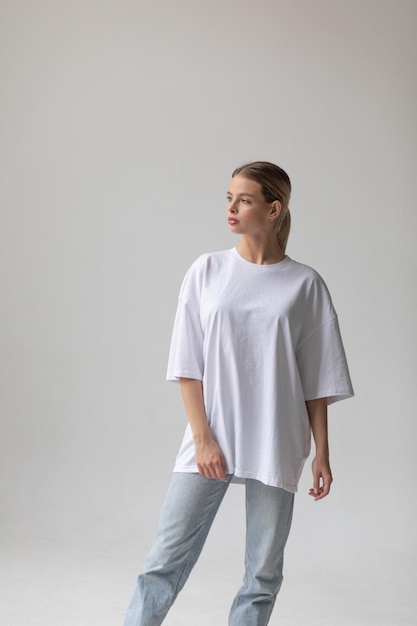 Free photo beautiful blonde girl in a white oversized tshirt and blue jeans posing on a gray background