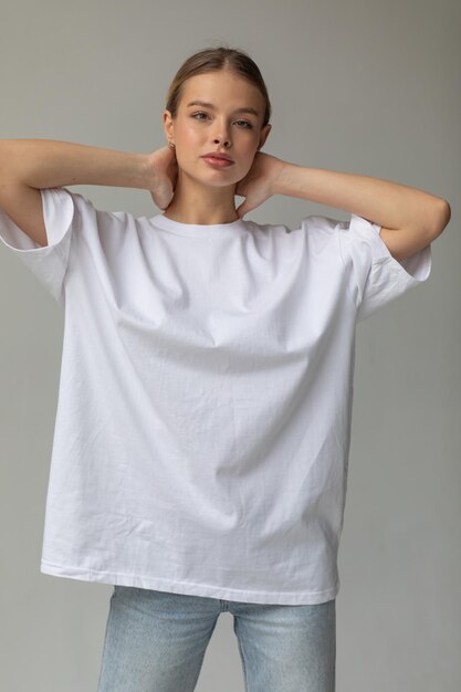 Beautiful blonde girl in a white oversized tshirt and blue jeans posing on a gray background