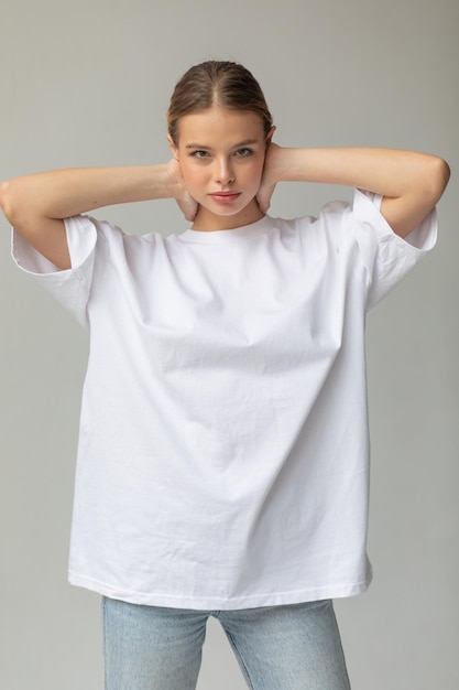 Free Photo beautiful blonde girl in a white oversized tshirt and blue jeans posing on a gray background