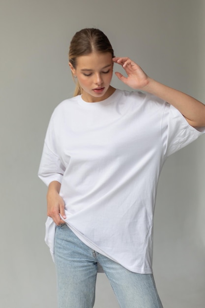 Free Photo beautiful blonde girl in a white oversized tshirt and blue jeans posing on a gray background