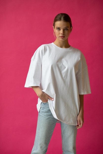 Free photo beautiful blonde girl in a white oversized tshirt and blue jeans posing on a gray background