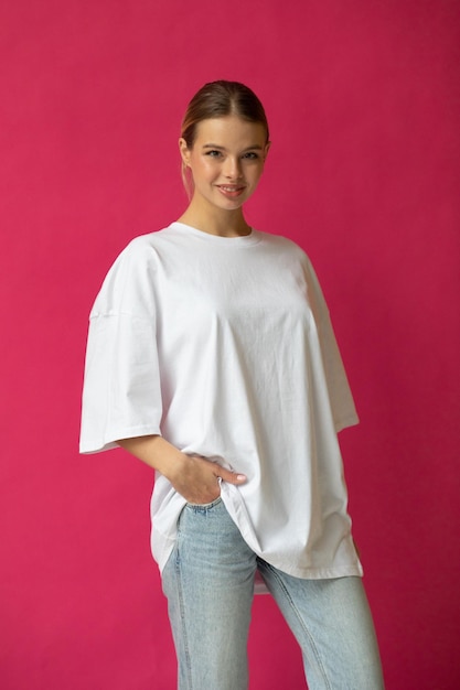 Free photo beautiful blonde girl in a white oversized tshirt and blue jeans posing on a gray background