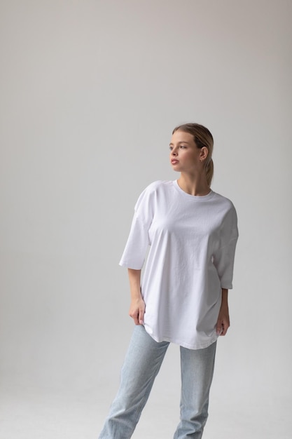 Free photo beautiful blonde girl in a white oversized tshirt and blue jeans posing on a gray background