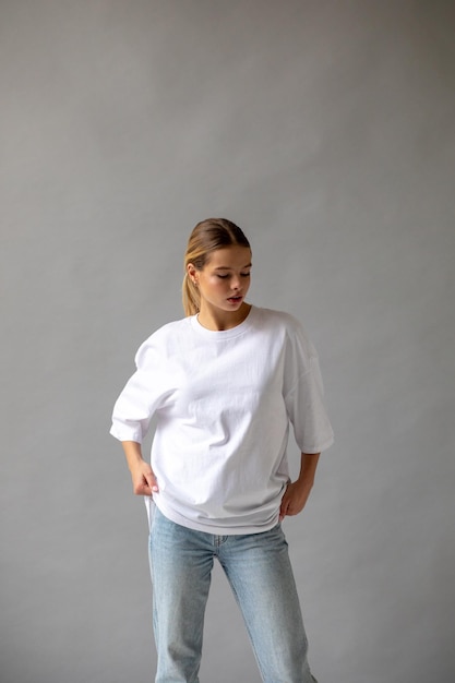 Free photo beautiful blonde girl in a white oversized tshirt and blue jeans posing on a gray background