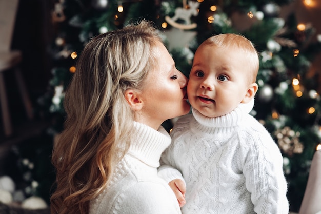 Free Photo beautiful blonde mother kissing her son's cheek against christmas tree.