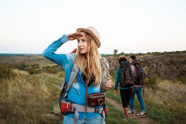 Beautiful blonde woman smiling, looking into distance, friends tourists background