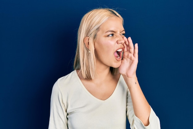 Free Photo beautiful blonde woman wearing casual sweater shouting and screaming loud to side with hand on mouth communication concept