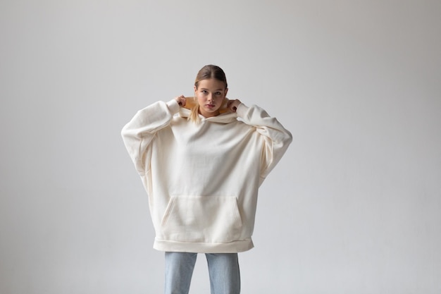 Free Photo beautiful blonde woman in a white hoodie and blue jeans posing on a white background