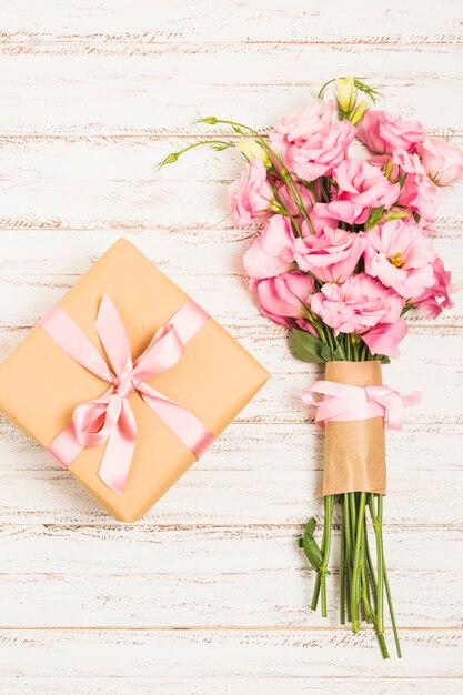 Beautiful bouquet of fresh pink eustoma flowers with present box on wooden surface