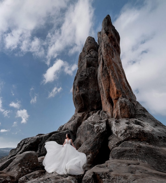 Beautiful bride is standing on the rock near the high cliff on the clear day with blue sky