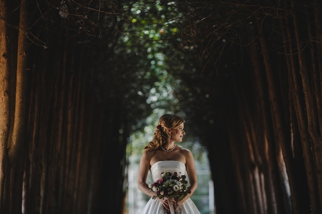 Free photo the beautiful bride with bouquet stands in the park