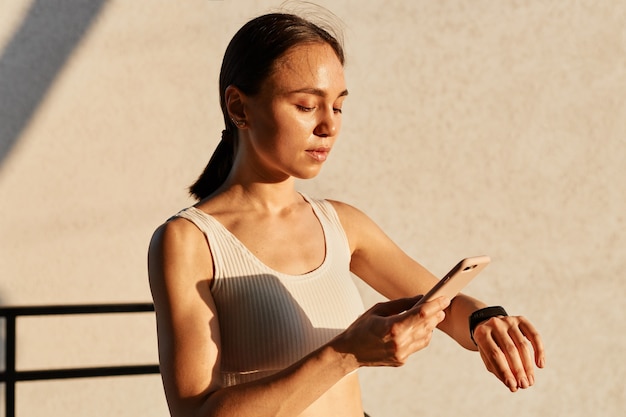 Free photo beautiful brunette female with ponytail wearing white top, connecting her smart phone